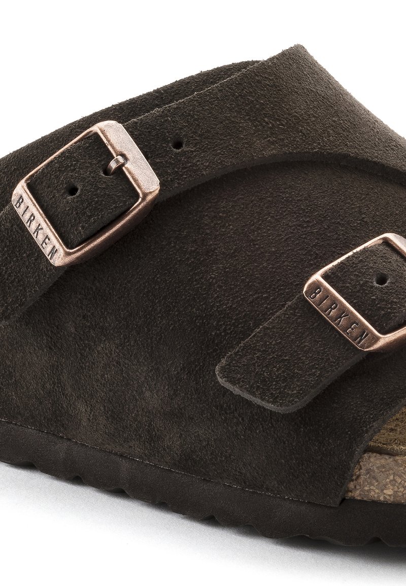 Sandale en daim brun avec deux sangles ajustables et boucles en ton cuivre. Surface texturée et semelle intérieure en liège avec une semelle en caoutchouc.