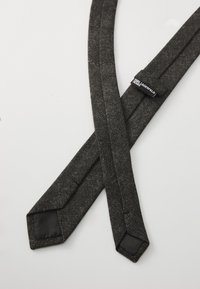 Black fabric suspenders with a textured finish, sharp angles, and black leather accents. Tag labels brand name.