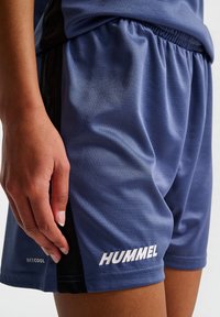 Blauwe sportshorts van ademend materiaal met een gestructureerde afwerking. Heeft een zwart zijpaneel en een wit "HUMMEL" logo. Elastische tailleband.