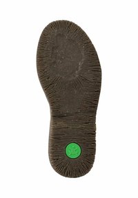 Suela de zapato de goma negra desgastada con un patrón de surcos lineales y un pequeño círculo verde con un logo de rana cerca del talón.