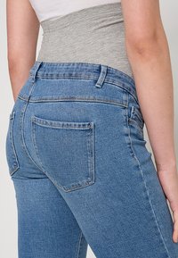 Modre kavbojke z visokim pasom iz jeansa z gladko teksturo, dvema zadnjima žepoma in nežnimi šivi. Pas je iz sivega blaga.