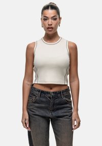 Top cropped beige con cuciture scure a contrasto, scollatura rotonda e design senza maniche, abbinato a jeans a vita alta in denim scuro.
