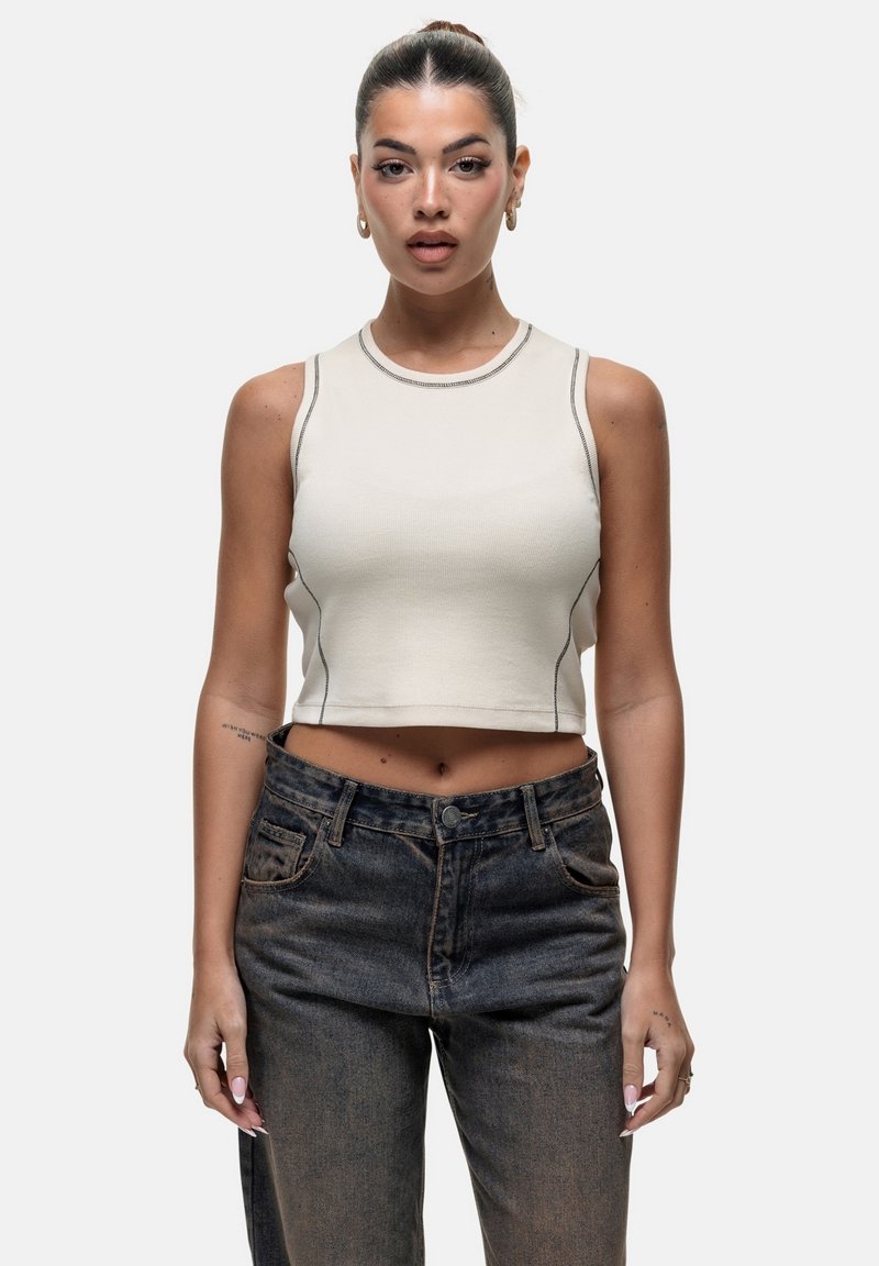 Top cropped beige con cuciture scure a contrasto, scollatura rotonda e design senza maniche, abbinato a jeans a vita alta in denim scuro.