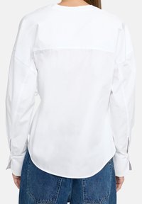 Biała koszula z długimi rękawami, charakteryzująca się zaokrąglonym dołem, zapiętymi mankietami oraz gładkim bawełnianym materiałem, przedstawiona z tyłu.