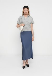 Maglietta corta in maglia grigia a maniche corte sovrapposta a una lunga gonna in satin blu, abbinata a scarpe nere con punta e una borsa bianca.
