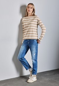 Beige gestreiftes Langarmoberteil mit einem U-Boot-Ausschnitt und geknöpften Manschetten, kombiniert mit hellblauen, gewaschenen Jeans und beigen High-Top-Sneakern.