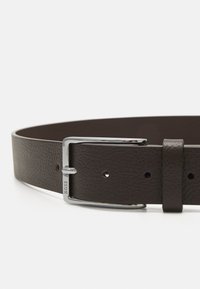 Ceinture en cuir marron avec une finition texturée, dotée d'une boucle en métal argenté et d'une sangle avec des trous pour l'ajustabilité.