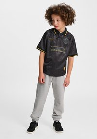 Svart kortärmad tröja med gula detaljer, strukturerat mönster och logotyp. Kombinerad med grå mjukisbyxor och svarta sneakers.