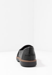 Chaussure en cuir noir à profil bas, arrière arrondi, coutures de semelle couleur tan, et texture lisse et brillante. Design simple sans ornements.