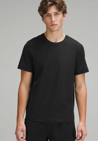 Tricou scurt cu mânecă închisă, dintr-un material moale, cu guler rotund, croială lejeră și un design minimalist, fără modele sau accente.