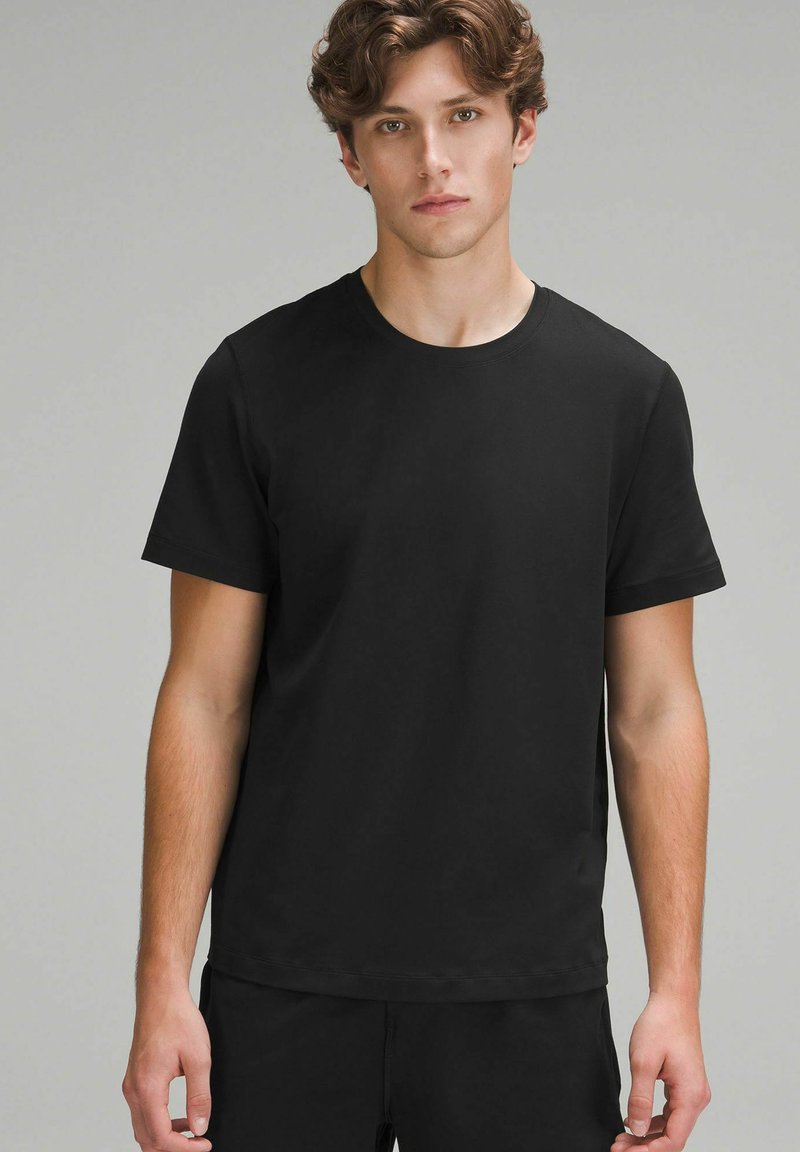 Tricou scurt cu mânecă închisă, dintr-un material moale, cu guler rotund, croială lejeră și un design minimalist, fără modele sau accente.
