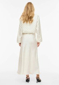 Robe à manches longues crème à pois noirs, avec une texture lisse et une silhouette fluide. Des chaussures noires basiques complètent le look.