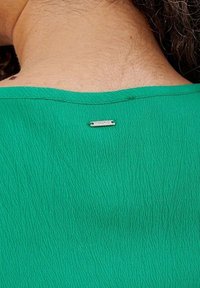 Groene gebogen stof top met een ronde halslijn, voorzien van een metalen label op de achterkant met de tekst "KARDINAL."