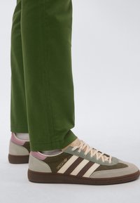 Πράσινο παντελόνι σε συνδυασμό με πολύχρωμα sneakers ρετρό στυλ που διαθέτουν ανοιχτό πράσινο, μπεζ και καφέ, με τρεις λευκές ρίγες και υφασματικές λεπτομέρειες.