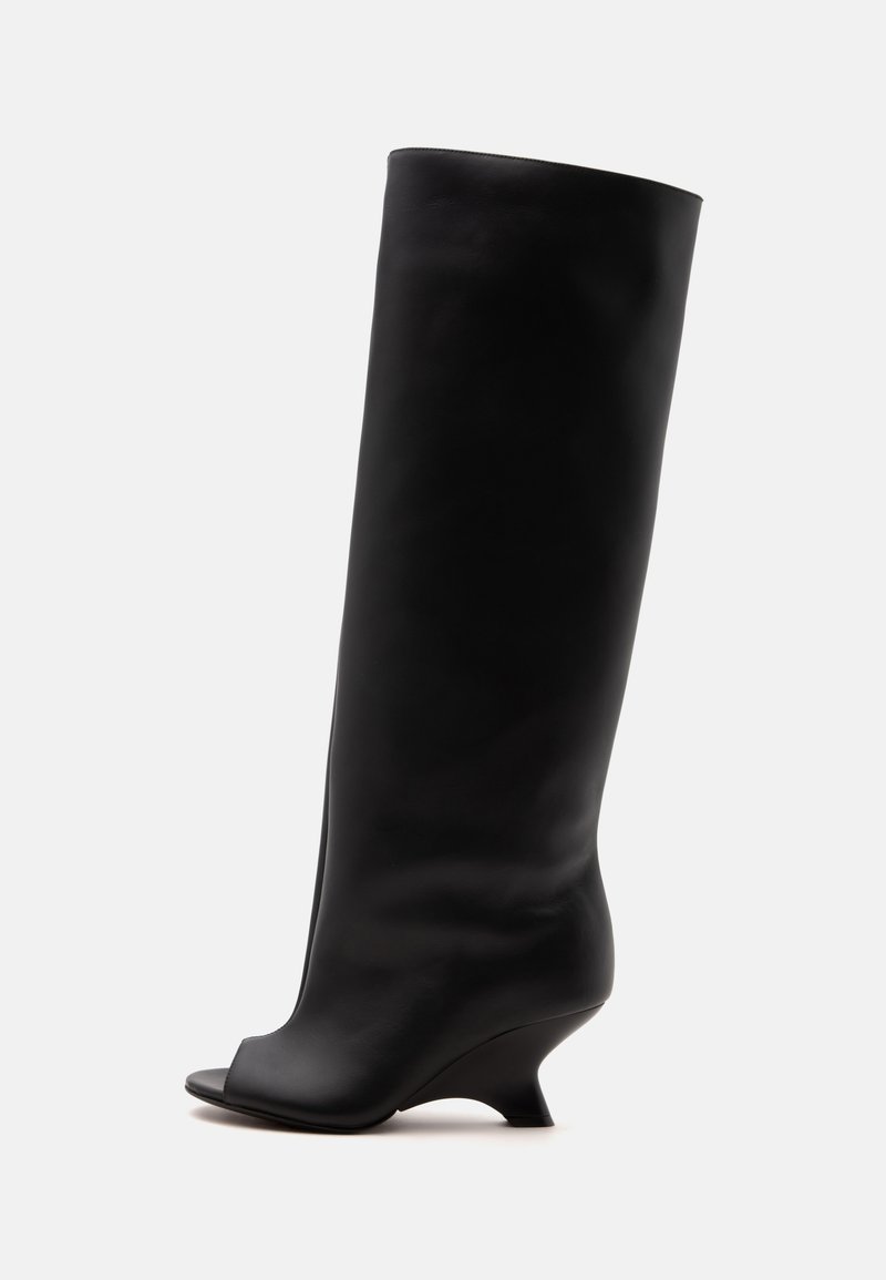 Botte en cuir noire montant jusqu'au genou avec un petit talon courbé et un bout ouvert sur fond blanc.