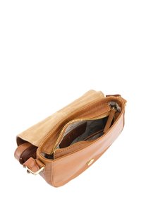 Tan læder crossbody taske med suedeflap, guld lynlås og indvendige lommer. Glat tekstur med kontrasterende materialer for design detaljer.