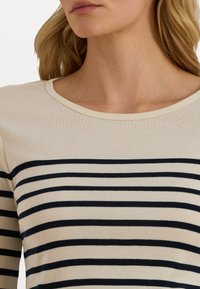 Top a maniche lunghe a righe in crema con righe orizzontali blu navy, caratterizzato da un collo arrotondato e una morbida trama a costine.
