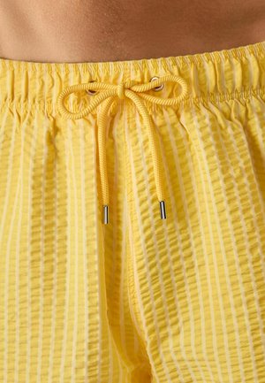 Nahaufnahme eines gelb gestreiften Bunds mit gebundenem Kordelzug an leichten Seersucker-Shorts.