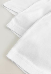T-shirts en coton blanc pliés, présentant des manches courtes et une texture lisse. Couture soignée visible le long des ourlets.
