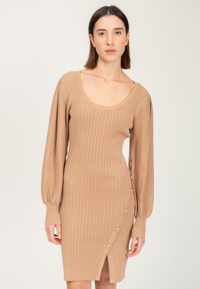 Beiges geripptes Strickkleid mit langen Ballonärmeln, Bootsauschnitt, seitlichem Knopfdetail und einem Oberschenkel-hohen Schlitz. Weicher Stoff und figurbetontes Design.