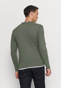 Langärmliges grünes Shirt aus weichem Stoff, mit rundem Halsausschnitt und taillierter Passform. Die Rückseite zeigt eine glatte Textur mit minimalen Nähte.