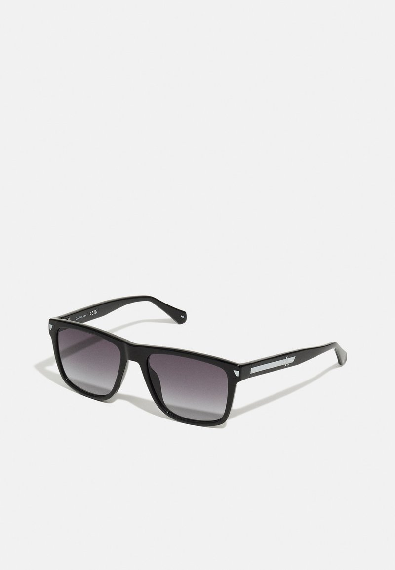 Óculos de sol de armação quadrada preta com lentes cinza em degradê, apresentando detalhes prateados nas hastes e textura plástica suave.