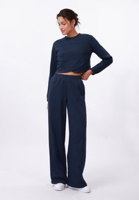 Un sweat-shirt cropped bleu marine présente un col rond et des manches longues. Associé à un pantalon large bleu marine, les deux étant en tissu doux.