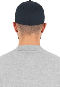 Zwarte pet met een ronde kroon, zichtbare stiksels en een gladde textuur, gedragen met een grijs poloshirt met een geribde kraag.