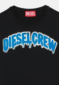 Crna majica s natpisom "DIESEL CREW" istaknutim podebljanim plavim slovima s efektom kapanja, obrubljena srebrnim metalik detaljima; dizajn s okruglim izrezom.