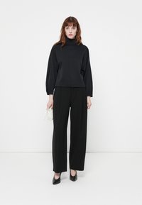 Maglione nero a collo alto con spalle cadenti, abbinato a pantaloni neri a gamba larga e décolleté neri a punta. Piccola borsa bianca come accessorio.