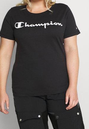 Personne portant un t-shirt Champion noir avec un logo blanc et un pantalon noir avec des poches boutonnées sur les cuisses.