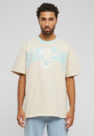 Beige cotton oversized t-shirt with turquoise crew neck and graphic print featuring the text "KARL KANI" and an eagle design.