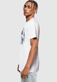 Hvid bomulds t-shirt med et blåt og rødt grafisk design med blomster detaljer på forsiden. Korte ærmer og afslappet pasform.