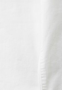 Tissu blanc avec une texture lisse, présentant des coutures subtiles. Le matériau semble léger et sans texture avec aucun motif visible.