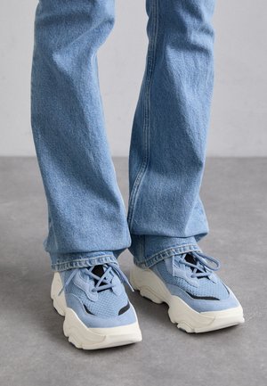 Lys blå sneakers laget av mesh og semsket skinn, med en kraftig hvit såle, sorte detaljer og snøring, kombinert med blå jeans.