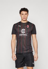 Čierne futbalové tričko s krátkym rukávom a červenými vertikálnymi prúžkami, logo Puma na ľavej hrudi a nápis "FUTBAL" vytlačený bielou farbou. Čierne šortky.