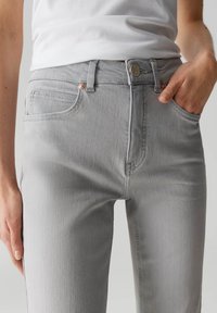 Jeans in denim grigio con una forma aderente, cinque tasche e accessori in tonalità rame, dotati di chiusura a bottone e tessuto leggermente testurizzato.