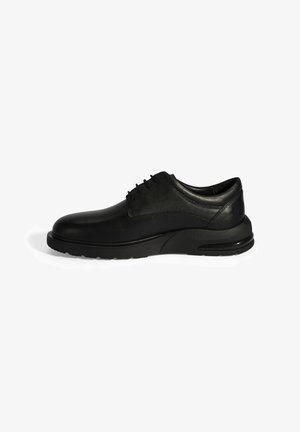 Chaussure en cuir noir avec un bout arrondi, un laçage, un col rembourré et une épaisse semelle en caoutchouc noir, présentant un léger talon pour un soutien supplémentaire.