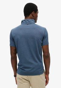 Polo azul de manga corta con cuello, confeccionado en tejido texturizado. Cuenta con una pequeña etiqueta de logo en la parte trasera y un diseño de ajuste relajado.