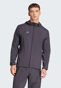 Black athletic jacket with hood, lightweight fabric, front zipper, side pockets, and a prominent Adidas logo on the chest.