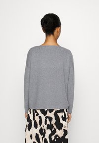 Grå stickad tröja med vid halsringning och långa ärmar, visad framifrån. Matchad med en mönstrad kjol med djurtryck.