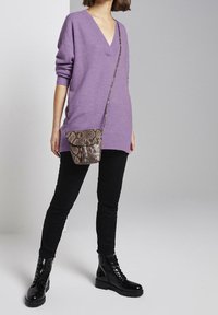Pull violet surdimensionné avec un col en V, associé à un jean skinny noir et des bottes de combat brillantes noires ; complété par un petit sac bandoulière en imprimé serpent marron.