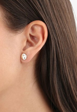 Pendientes de aro de oro con una superficie lisa y redonda, que presentan un pequeño diseño de estrella y forma circular. Mostrados en la oreja de un modelo.