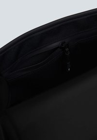 Interno della borsa nera caratterizzato da un materiale liscio, una tasca con zip e fodera in rete, con un robusto tirazip e cuciture rinforzate.