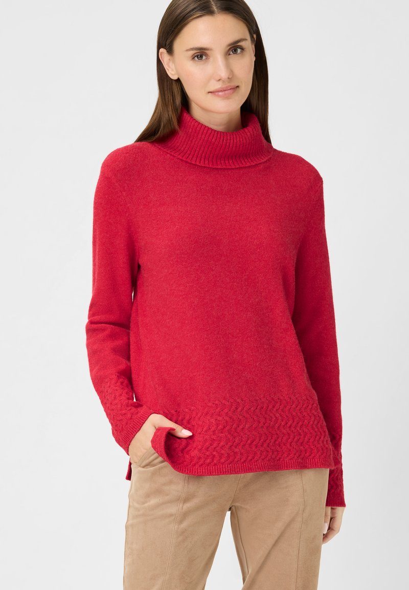 Roter Pullover mit geripptem Rollkragen und einem strukturierten Zickzackmuster entlang des unteren Saums. Hergestellt aus weichem Strickstoff.