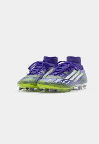 Ciorapi de fotbal vibranti de culoare violet, cu accente verzi, având un design elegant, material texturat și un guler înalt pentru susținere.