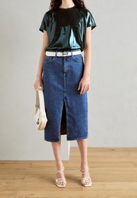 Skinande mörkgrön t-shirt, vit bälte, blå denimkjol i medellängd med framslits, och ljusa sandaletter med remmar. En enkel, avslappnad outfit.