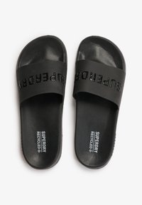 Zwarte slippers van gerecycled materiaal, met een textuurafwerking, opvallende "SUPERDRY" branding op de band en een platte zool.