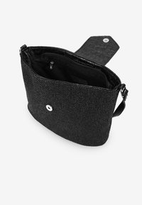 Bolso de mano negro tejido con una textura suave, cierre de solapa en la parte superior y un botón de presión plateado. Cuenta con un compartimento interior con cremallera.