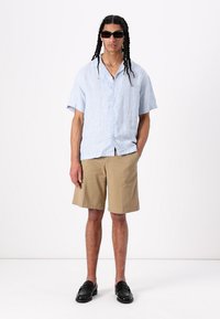 Hellblau gestreiftes Kurzarmhemd, beige Shorts, schwarze Slipper und Sonnenbrille; lockere Passform, mit Knöpfen.